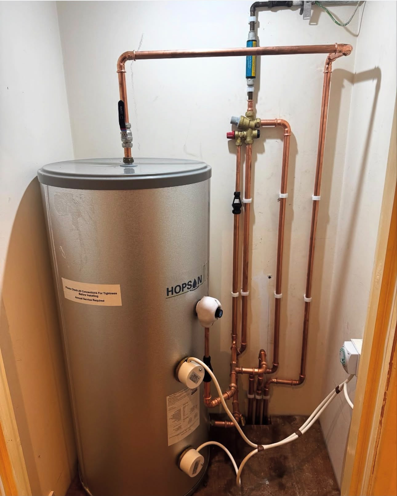 Unvented hot water cylinder installation with neat copper pipework routed in a compact cupboard